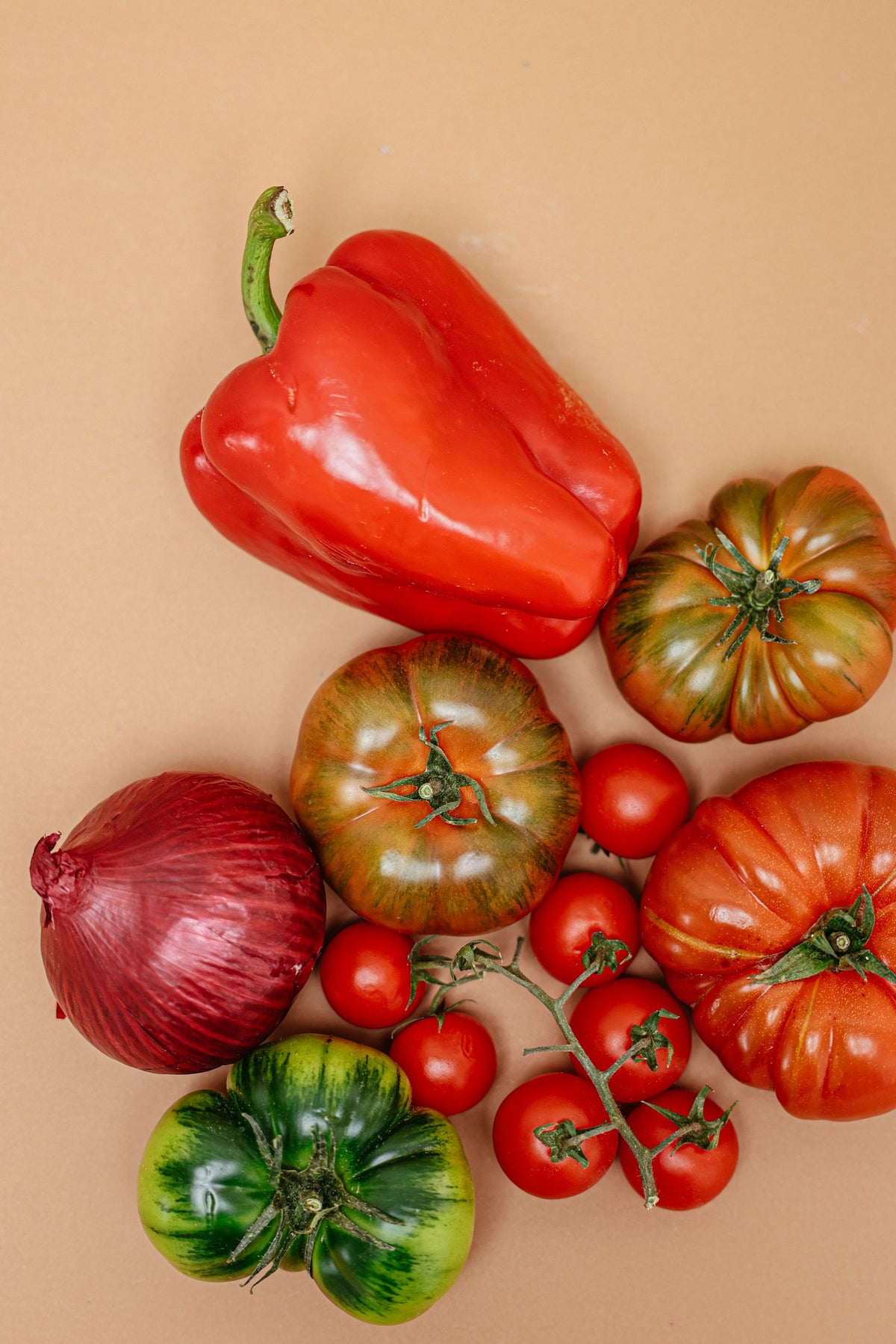 Close-up of fresh heirloom tomatoes and a bell pepper on a beige surface